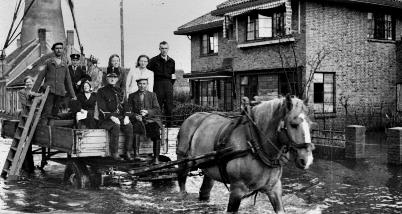 Paard en wagen rijden door Souburg tijdens de inundatie: het paard loopt tot de buik in het water, mensen staan op de kar